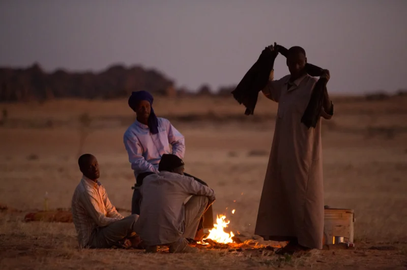 A group of Toubou travelers warms up around a fire in the evening, in the Ennedi desert.