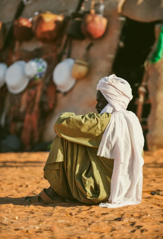 Un homme touareg se repose près de son campement, entouré par les éléments du désert. Une scène de calme et de sérénité au coeur du Sahara.